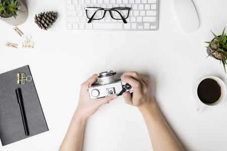 Man is holding an old vintage film camera over the white desk table top view flat lay Stock Photo