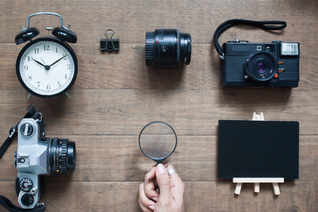 Top view of photographer desk with woman s hand holding magnifying glass wooden background Stock Photo