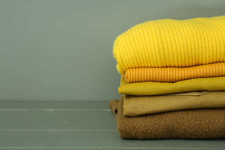 Stack of warm clothes on table against color background Stock Photo