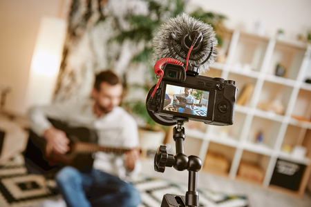 Learning guitar male music blogger sitting on the floor at home and recording new guitar lesson with camera on foreground