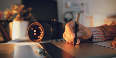 Graphic designer working on digital tablet camera on desk in background photographer working at office