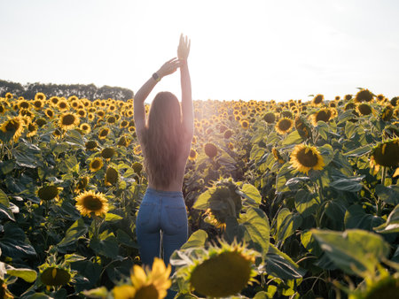 Imagen hermosa y soleada de una joven mujer alegre sosteniendo las manos en el aire y mirando el amanecer o el atardecer. Stand solo entre campo de girasoles. Disfruta el momento.