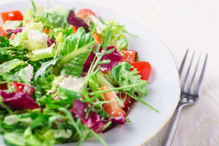 Fresh salad with green and purple lettuce tomatoes and cucumbers on white wooden background close up healthy food Stock Photo