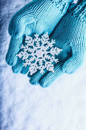 Female hands in light teal knitted mittens with sparkling wonderful snowflake on a white snow background winter and christmas cozy concept Stock Photo