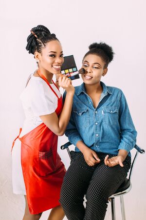 Young beautiful african american woman applying professional make up by african make up artist studio shoot