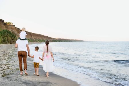 Familia de cuatro personas caminando por la orilla del mar. Padres y dos hijos. Vista trasera