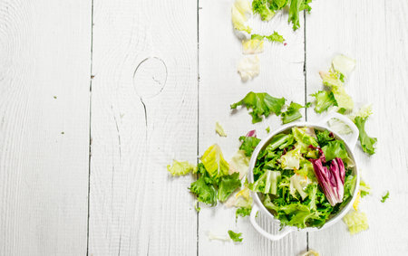 Fresh salad greens in a bowl on a white wooden background