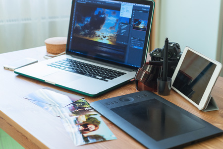 Work space or desktop hipster photographer in the sunlight from the window laptop film camera film roll tablet and several lenses on a wooden table