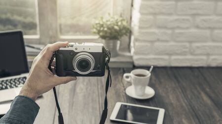 Hipsterski fotograf w domu siedzi przy biurku i robi sobie selfie aparatem, strzał z punktu widzenia