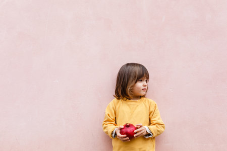 Niña con cabello rubio sosteniendo granada roja en sus brazos Foto de archivo