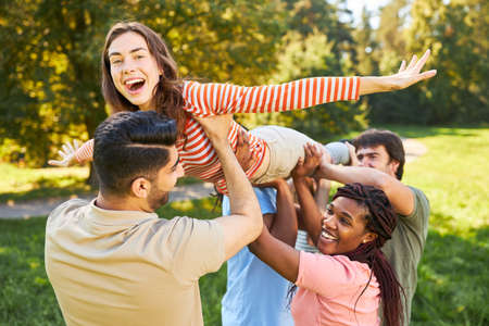 Un grupo de amigos juntos levanta a una mujer joven como un ejercicio de confianza y trabajo en equipo