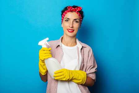 Mujer sonriente joven sosteniendo spray en guantes sobre fondo azul.