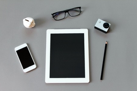 Business or work day background concept workspace desk with tablet computer pencil eye glasses small action camera piggy bank and smart phone on gray background Stock Photo