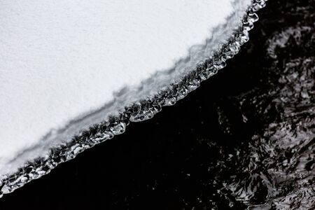 A close up of ice crystals forming between snow and a river Фото со стока