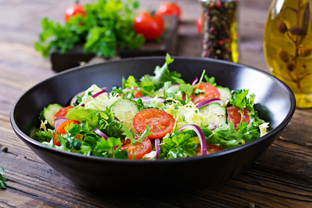 Salad from tomatoes cucumber red onions and lettuce leaves healthy summer vitamin menu vegan vegetable food vegetarian dinner table