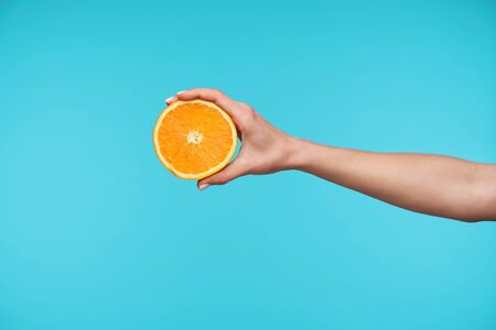 Studio photo of elegant pretty hand keeping half of fresh orange while posing against blue background going to make fresh juice for breakfast