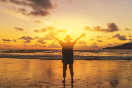 Una mujer feliz levanta la mano en una playa tropical con fondo de cielo al atardecer. Las vacaciones de viaje y la libertad son un buen concepto. Estilo de color de efecto de filtro de tono vintage. Foto de archivo