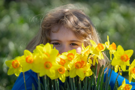 Little kid smelling spring narcissus flower outdoor child play in spring garden kids face near blooming cherry tree happy child during spring blossom