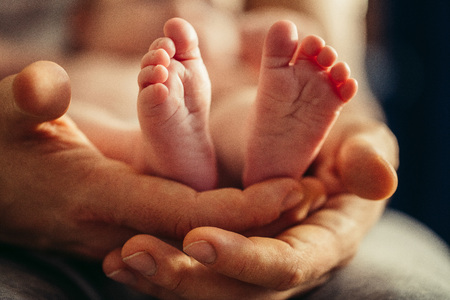 Newborn baby legs in mothers lovely hand with soft focus on babies foot Фото со стока