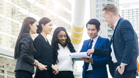 Team of business multi internationality people smart man and woman talk and present the project work with the paper work on the hand in good feeling at outdoor pedestrian walk way the city space modern building Stock Photo