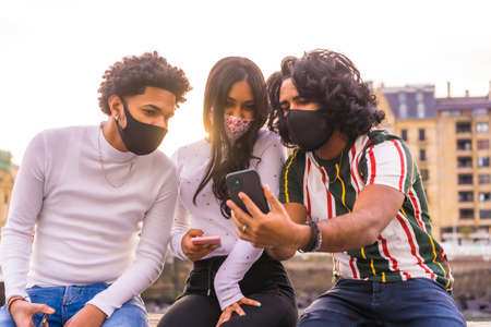 Estilo de vida, tres amigos latinos negros viendo las redes sociales en la calle con máscaras faciales. Amistades en la pandemia del coronavirus, covid-19. Distancia social, responsabilidad social, nueva normalidad