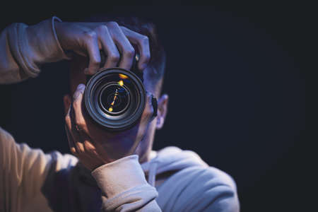 A man photographer with a camera takes a photo in the dark copy space