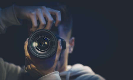 Mężczyzna fotograf z aparatem robi zdjęcie w ciemności, kopiując przestrzeń.