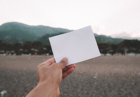 Nota de papel vacía en la mano sobre fondo de paisaje increíble. Concepto de viajes y vacaciones. Trozo de papel blanco sin texto