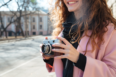 Cropped image of a smiling woman in coat holding retro camera in hands