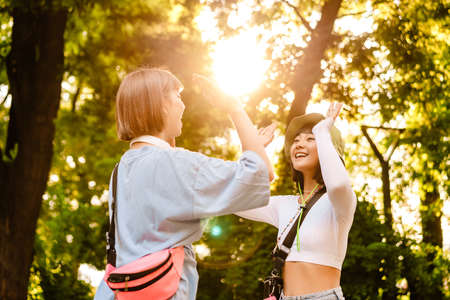 Dos mujeres multirraciales sonriendo y chocando los cinco mientras caminan juntas en Green Park Foto de archivo