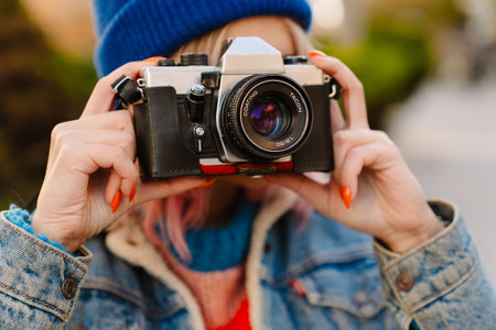 Young woman taking photo on retro camera while walking in park outdoors Stock Photo