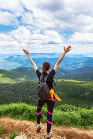 Una joven con una mochila, con las manos levantadas sobre un fondo de hermosas montañas y un hermoso cielo nublado. Ocio. Senderismo. Estilo de vida saludable.