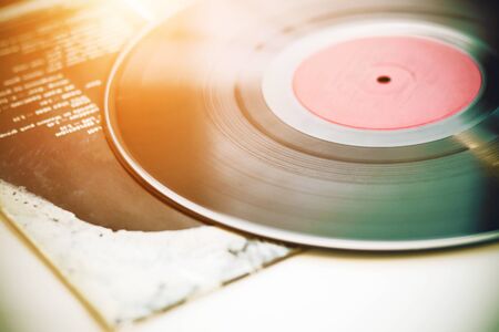 Un disco de vinilo negro musical antiguo se encuentra en la cubierta de papel de un álbum de música, iluminado por la luz del sol.