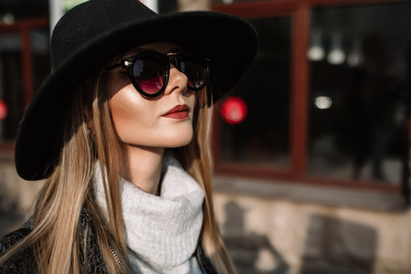Portrait of a young beautiful fashionable girl wearing sunglasses model in a stylish black hat harmoniously similar clothes in gray tones street style women s fashion Stock Photo