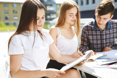 The guy student explains to the girls something and shows in a notebook portrait of three happy high school students students friends learn do homework together spend time and have fun Stock Photo