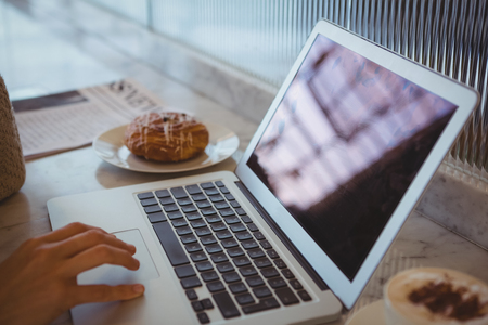 Cropped hand of woman using laptop at counter in cafe Stock Photo