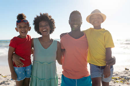 Retrato de una familia afroamericana sonriente con los brazos alrededor disfrutando de las vacaciones de verano en la playa. inalterado, familia, estilo de vida, unión, disfrute y concepto de vacaciones.