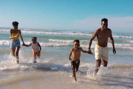 Alegres padres jóvenes afroamericanos sosteniendo las manos de los niños y corriendo en el mar contra el cielo. feliz, naturaleza, verano, inalterable, playa, infancia, familia, unión, disfrute, vacaciones.