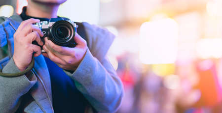 Asian female traveller smile happiness hand hold mirrorless camera enjoy nightlife lifestyle tourost with light bokeh and crowd of people blur background in winter season close up banner size Stock Photo