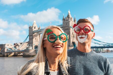 Pareja feliz con gafas de Navidad en Londres - Joven pareja caucásica divirtiéndose en Londres el día de Navidad, Tower Bridge en segundo plano - Vacaciones y conceptos de estilo de vida