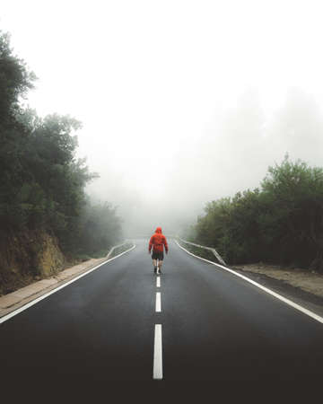 A vertical shot of a male walking through the highway covered by fog leave everything behind concept