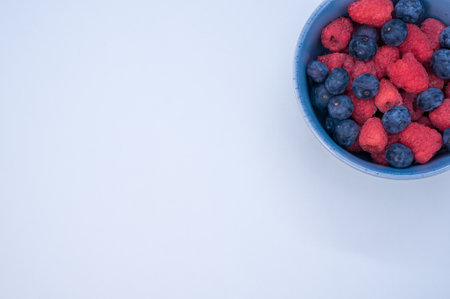 A bowl of fresh berries isolated on a blue background with space for text Stock Photo