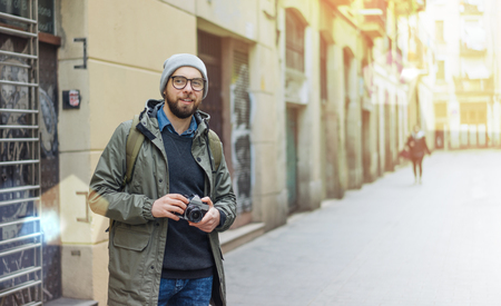 Male casually dressed bearded tourist with a backpack walking through the old town street with retro film photo camera traveling and freelance concept