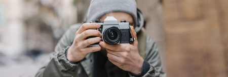 Male casually dressed bearded tourist with a backpack taking photo with retro film photo camera on the old town street traveling and freelance concept close up cropped shot Stock Photo