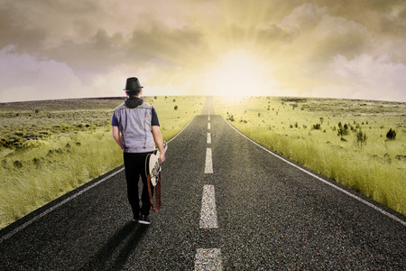 The lonely guitarist walking on road shot outdoors at dusk Stock Photo