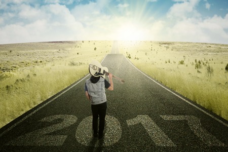 Rear view of young male holding a guitar and standing on the road with numbers 2017