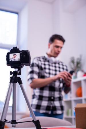 Talking to audience dark haired young man shooting new video for his channel while professional camera standing on tripod