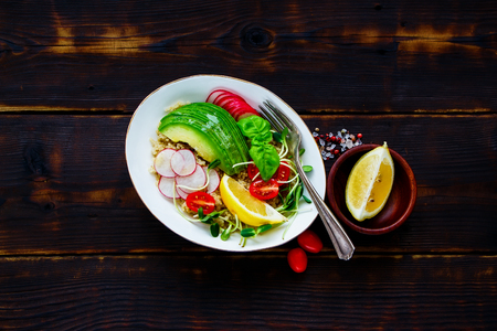 Bowl of homemade quinoa salad with sprouts tomatoes avocado radish and basil on dark rustic wooden background top view detox dieting vegan vegetarian clean eating concept Stock Photo