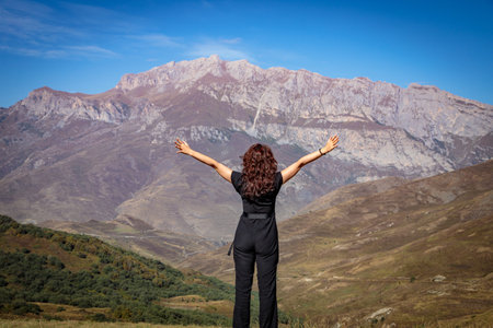 A young woman stands on top of a mountain with her arms outstretched