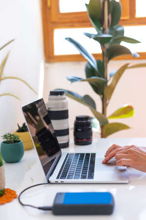 Photographer s workplace laptop and camera lenses on a white table photographer concept with digital camera external harddisk hands on keyboard close up